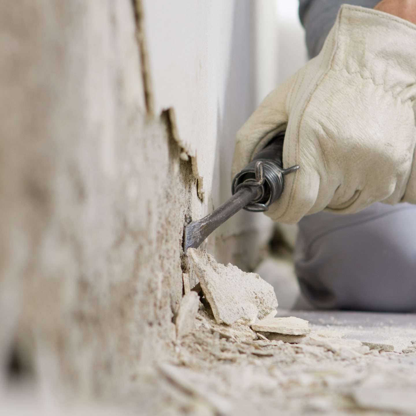 house renovation concept, construction worker breaks the old plaster of the wall with pneumatic air hammer chisel, close up with rubble on floor