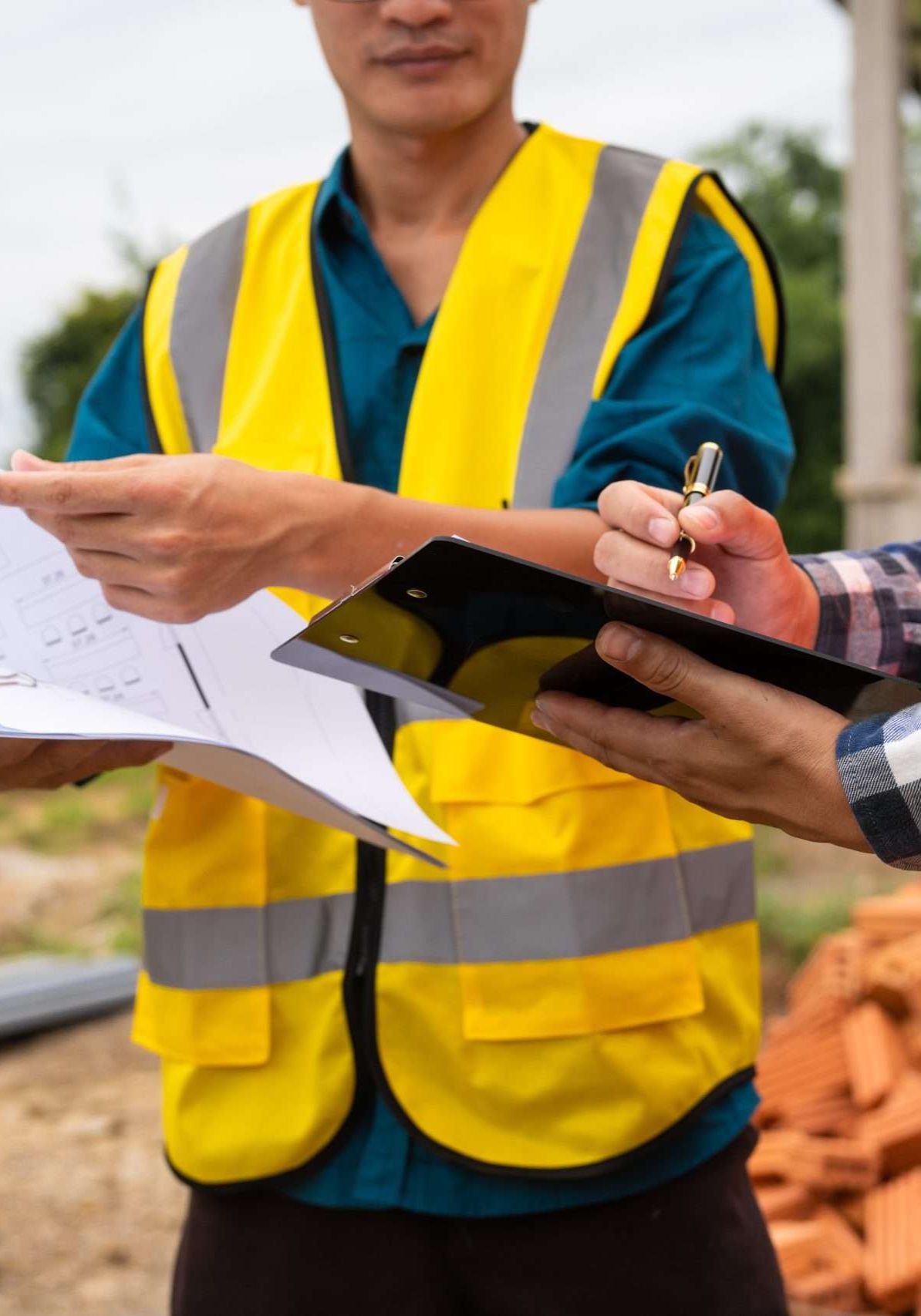 Two male architects wearing hard hats and safety vests discuss construction design on-site.collaborating with the contractor on the house structure, including iron framework, brickwork, and roofing.